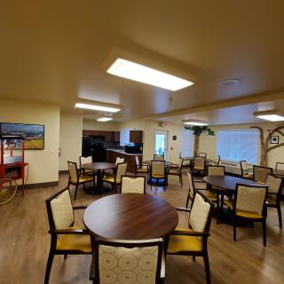 A spacious dining room with multiple tables and chairs, featuring wood flooring and ample lighting.