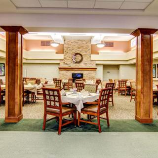 A well-lit dining area with neatly arranged tables and chairs, featuring a stone fireplace as the focal point.