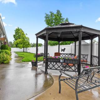 A backyard featuring a metal gazebo with seating, surrounded by a lush green lawn and a paved pathway.