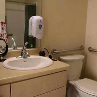 A clean bathroom with a sink, mirror, toilet, and soap dispenser.