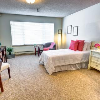 A cozy bedroom featuring a single bed, comfortable chairs, and large window.