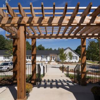 A wooden pergola casts shadows over a walkway leading to residential buildings.