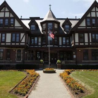 A beautiful historical building with a well-kept garden and an American flag in front.