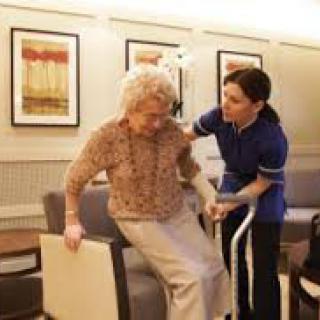 A caregiver assisting an elderly person in a living room setting.