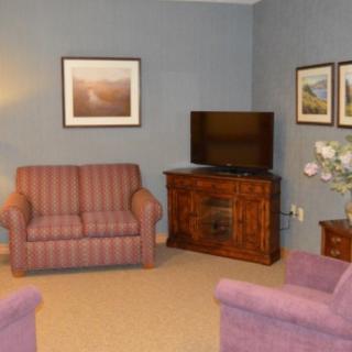 A cozy living room with two armchairs, a sofa, a television on a wooden cabinet, and framed pictures on the wall.