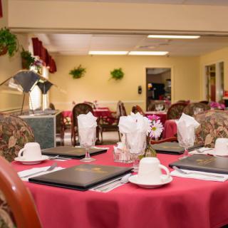 An elegantly set dining table in a restaurant with red tablecloths and tea cups.