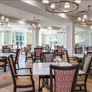 An elegant dining room with neatly arranged tables and chairs, illuminated by chandeliers.
