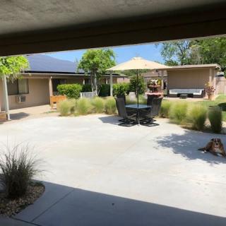 A sunny outdoor patio area with furniture, a sunshade, and surrounding garden landscaping.