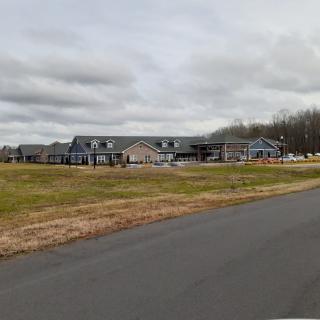 A large building under construction on a cloudy day with an adjacent road and open grassy area.