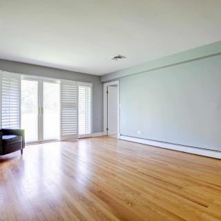 A spacious, sunlit room with hardwood flooring and large windows.