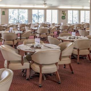 An empty dining room with neatly arranged chairs and tables on a carpeted floor.