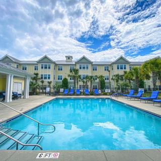 A luxurious outdoor swimming pool with a building and palm trees under a blue sky.