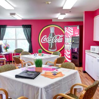 A vibrant dining area featuring a Coca-Cola themed decor with tables, chairs, and a vending machine.