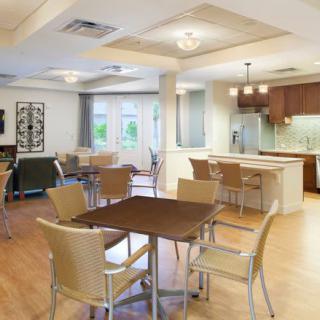 A modern dining room with adjacent kitchen area, featuring wooden floors, contemporary furniture, and elegant lighting.