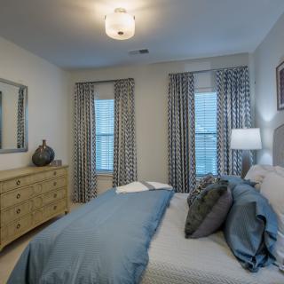 A modern bedroom with a neatly made bed, stylish curtains, and elegant lighting.