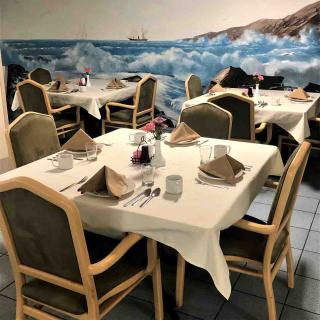 A restaurant dining area with neatly set tables and a scenic ocean mural on the wall.