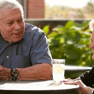 An elderly couple enjoying a conversation outdoors over drinks on a sunny day.
