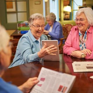 A group of seniors enjoying a social gathering, using a tablet and reading materials.