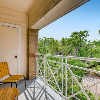 A peaceful balcony with seating and a view of lush green trees.