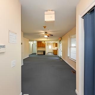 A view of a spacious living area with carpeted floors, a ceiling fan, and multiple windows.