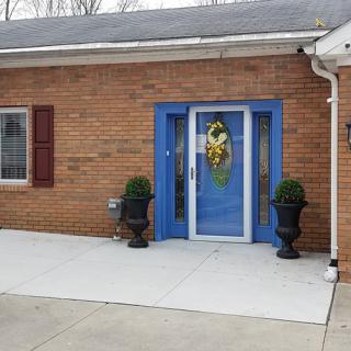 The front entrance of a brick building features a vibrant blue door with a decorative wreath and two black planters on either side.