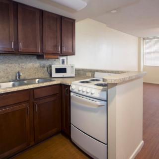 A compact kitchen area in an apartment featuring wooden cabinets, a stove, microwave, and sink.