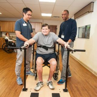 A person receiving support during a physical therapy session with two therapists assisting.