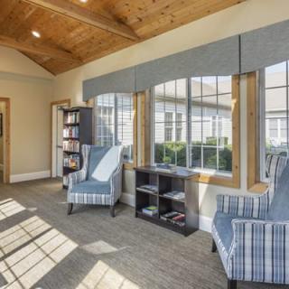 A bright sunroom with large windows, two striped chairs, and a bookshelf, accented by a wooden ceiling.