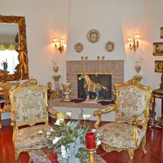 A classic living room with ornate furniture and a fireplace, featuring decorative mirrors and elegant armchairs.