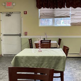 An empty dining area in a restaurant, featuring tables with green tablecloths and a view of the outside through a window.