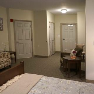 A cozy bedroom featuring a bed, chair, and small table, with multiple doors leading out of the room.
