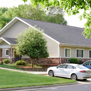 A suburban house with a well-maintained lawn and parked cars in the driveway.
