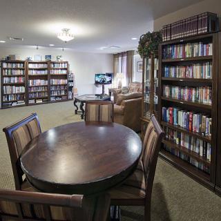 A cozy library reading area with bookshelves, tables, and chairs.