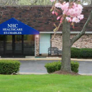 The entrance of NHC Healthcare in St. Charles, surrounded by blooming trees and a well-kept lawn.