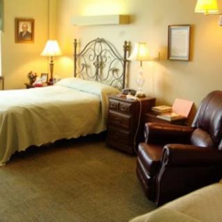 A cozy bedroom with a neatly made bed, lamps, and a comfortable armchair.