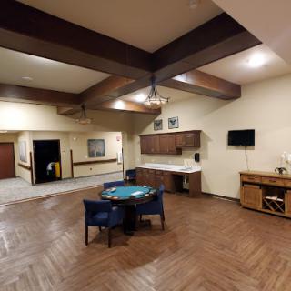 A spacious room featuring wooden beams, a dining table, and a kitchenette.