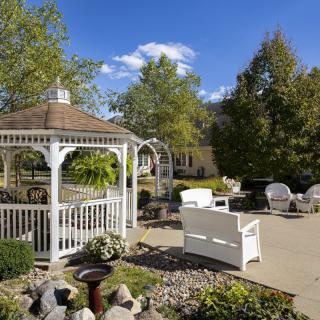 A peaceful garden setting with a white gazebo and outdoor seating on a sunny day.