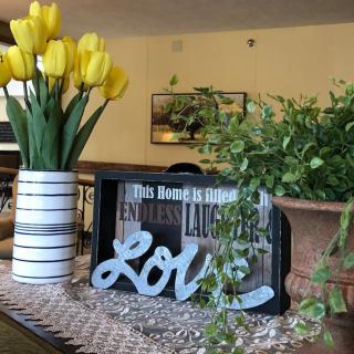 A cozy home decor setup featuring a vase of yellow tulips, a decorative love sign, and greenery.