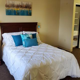 A cozy bedroom with a neatly made bed featuring blue accent pillows and a white comforter, complemented by wall art.