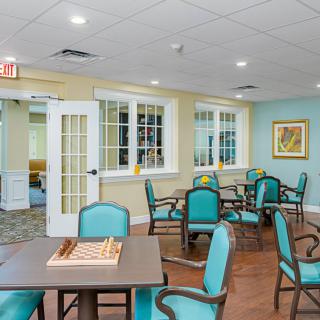 A well-lit dining area with teal chairs and tables, featuring a chess board on one of the tables.
