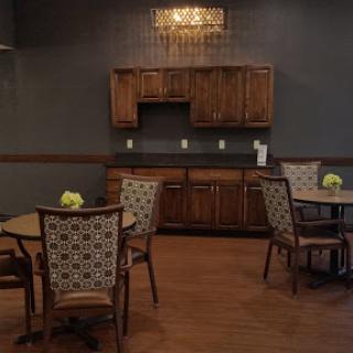 A cozy dining area featuring wooden furniture, a kitchenette, and decorative flowers.