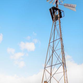 A tall windmill standing against a clear blue sky with scattered clouds.