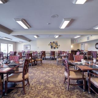 A spacious dining room with multiple tables and chairs, featuring a carpeted floor.