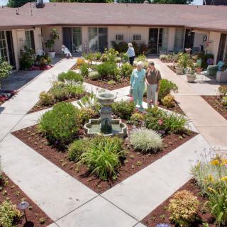A well-maintained courtyard garden with a central fountain, surrounded by pathways and various plants.
