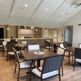 A modern dining area with tables and chairs arranged neatly in front of a kitchen counter.