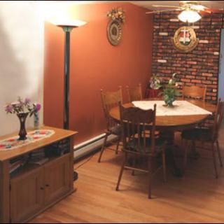 A cozy dining room with a wooden round table and chairs, decorated with a flower vase and surrounded by warm lighting.