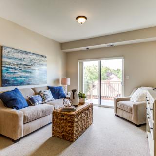 A cozy living room with a sofa, armchair, and coffee table, featuring artwork and abundant natural light through a sliding glass door.
