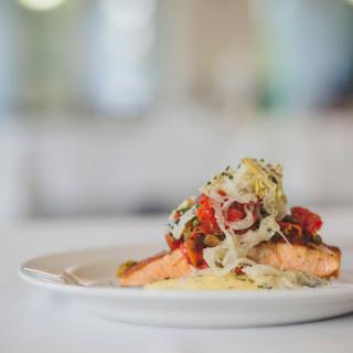 A beautifully plated salmon dish topped with colorful vegetables.
