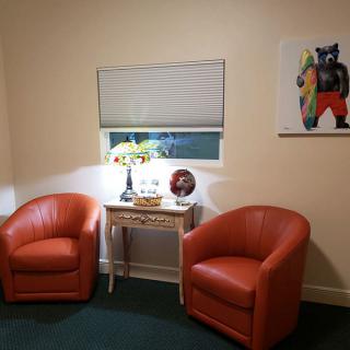 A cozy room with two orange chairs and a small table, featuring a window and colorful artwork on the wall.