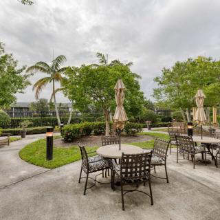 An inviting outdoor patio area with tables, chairs, and umbrellas surrounded by lush greenery.
